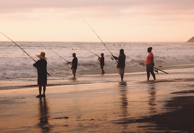 isherman casting a line into the ocean during the Australian Salmon Fishing Championships, with waves and coastal scenery in the background.